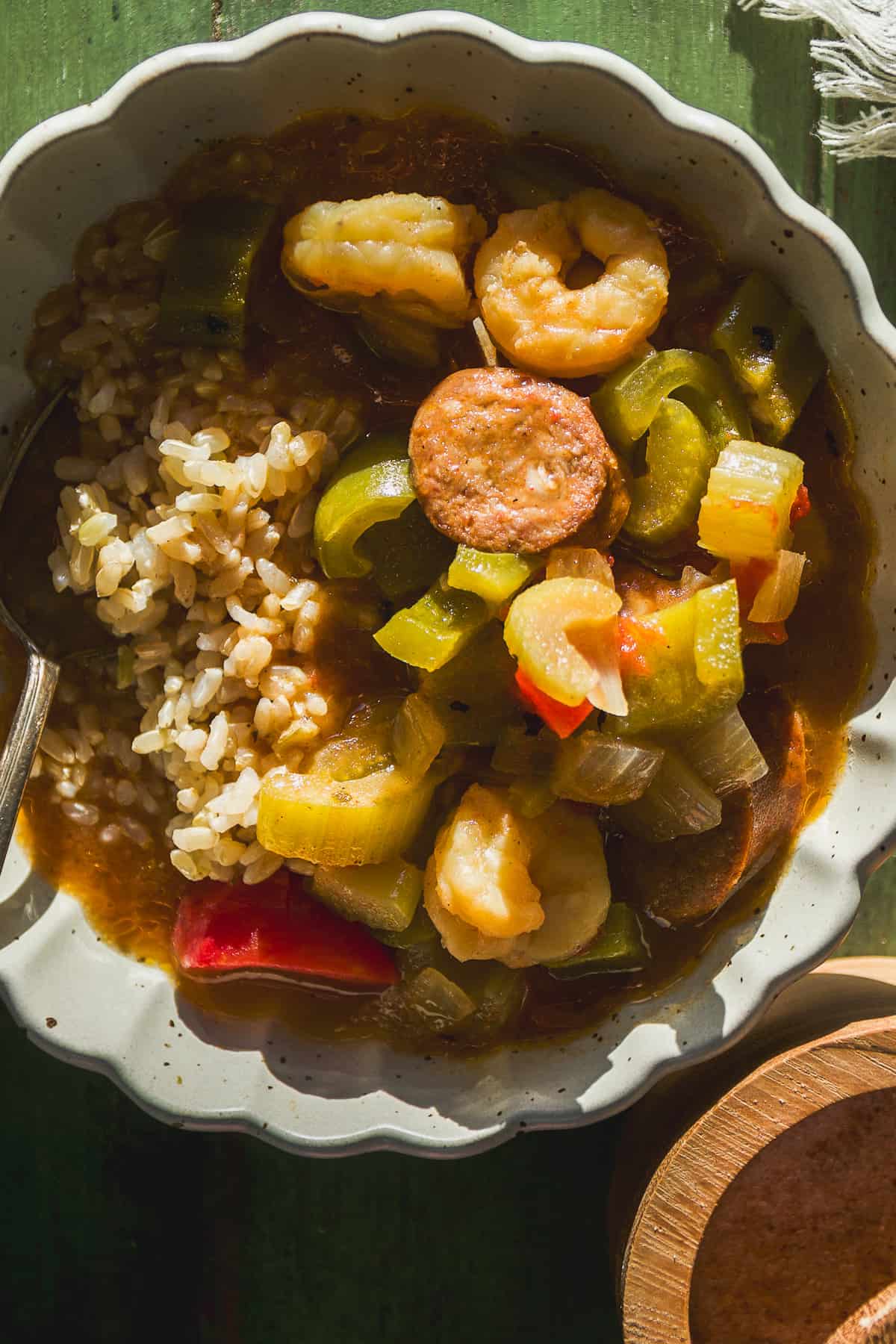 Gumbo with brown rice in a shallow bowl with a spoon.