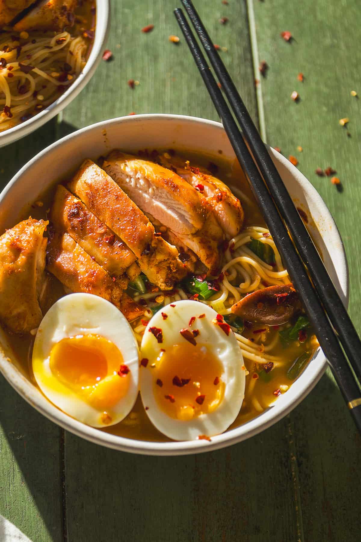 Chicken ramen noodles in a bowl with a soft boiled egg and chopsticks.