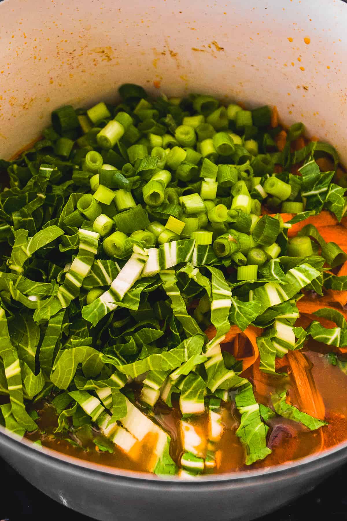 Bok choy and green onions in a ramen pot with broth.