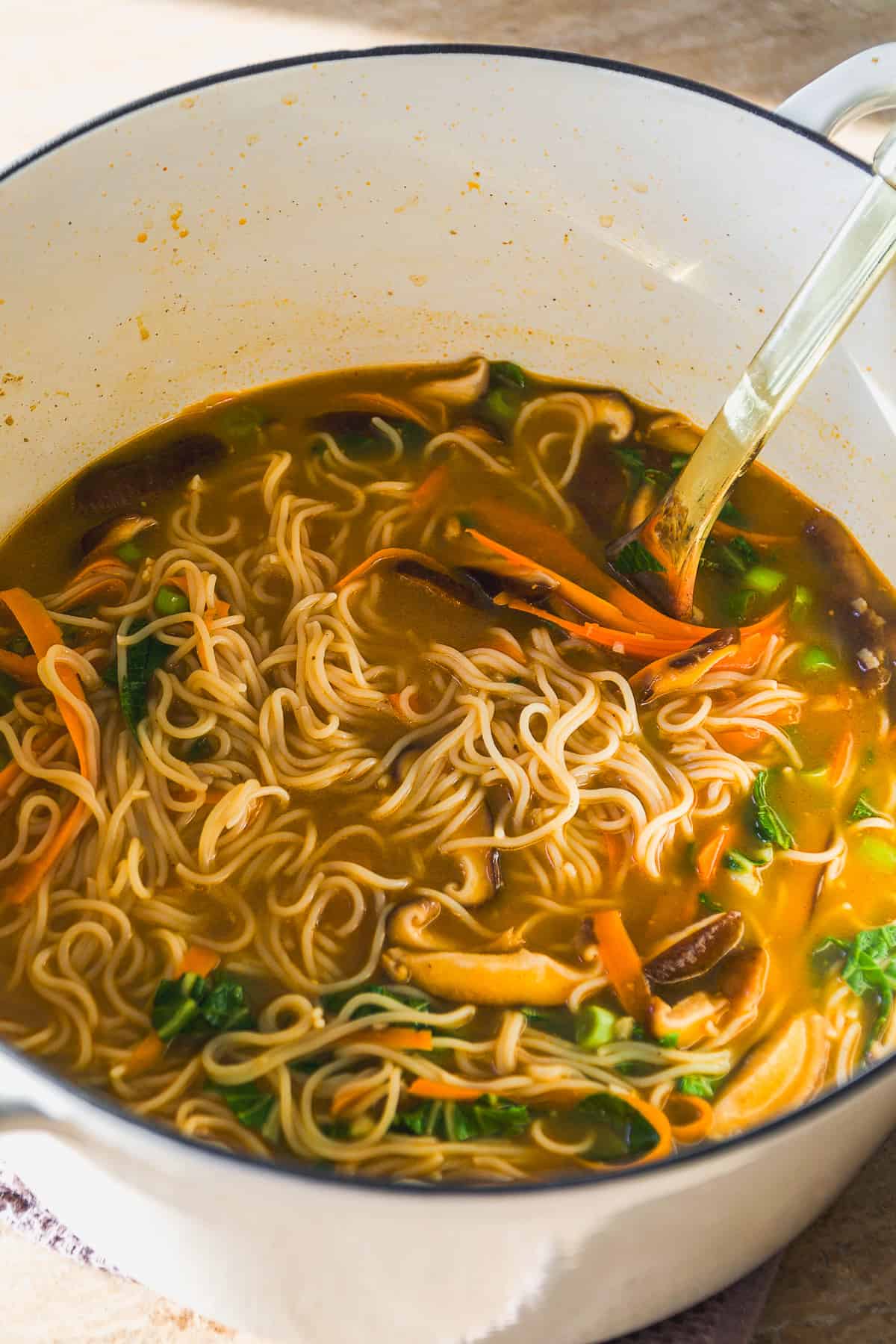 Ramen noodles in a pot with bok choy and carrots and veggies.