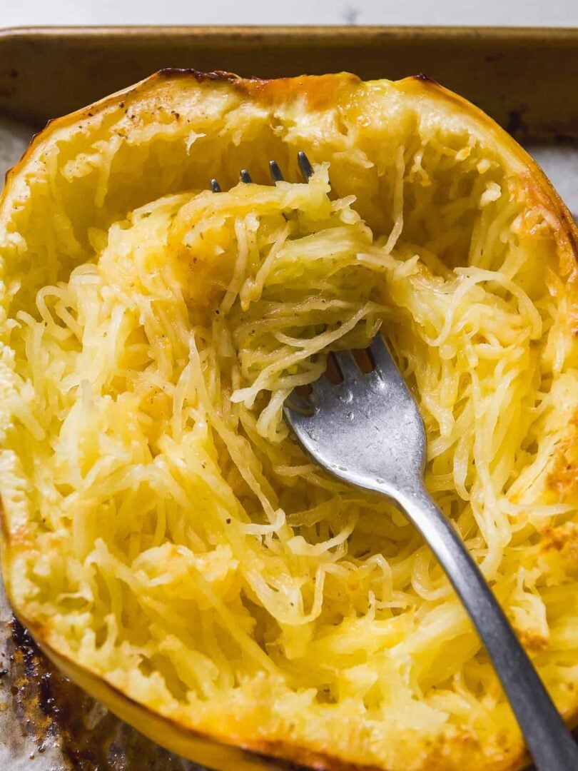 Roasted spaghetti squash with a fork pulling the strands from the skin.