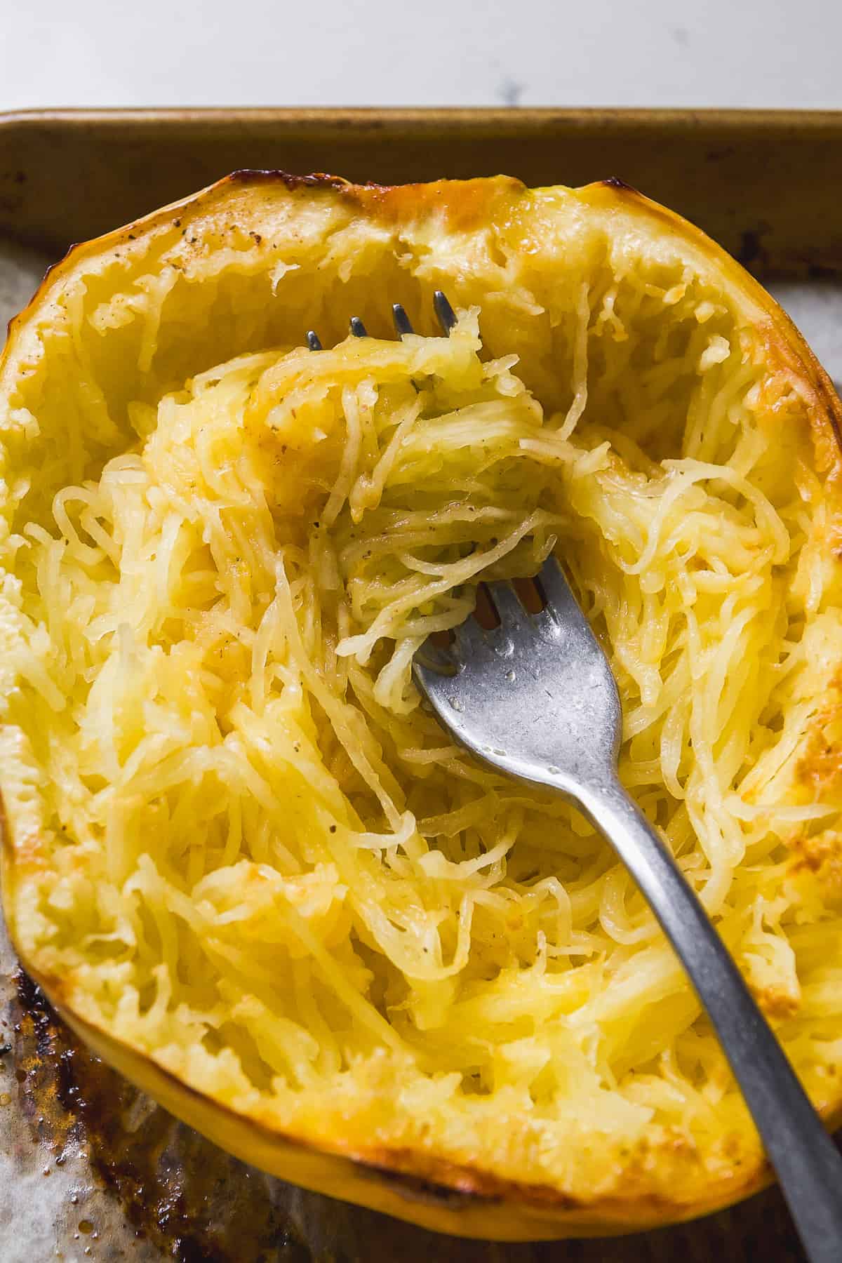 Roasted spaghetti squash with a fork pulling the strands from the skin.