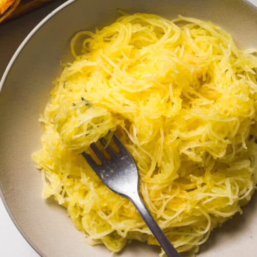 Spaghetti squash stands in a tan bowl with a fork.