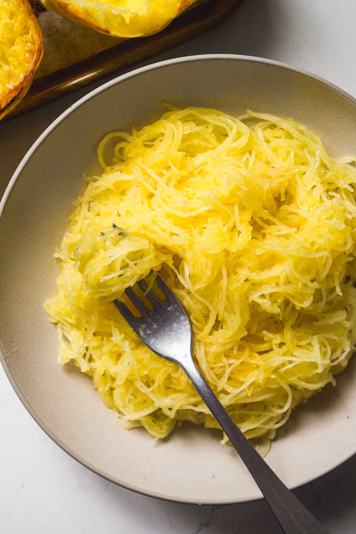 Spaghetti squash stands in a tan bowl with a fork.