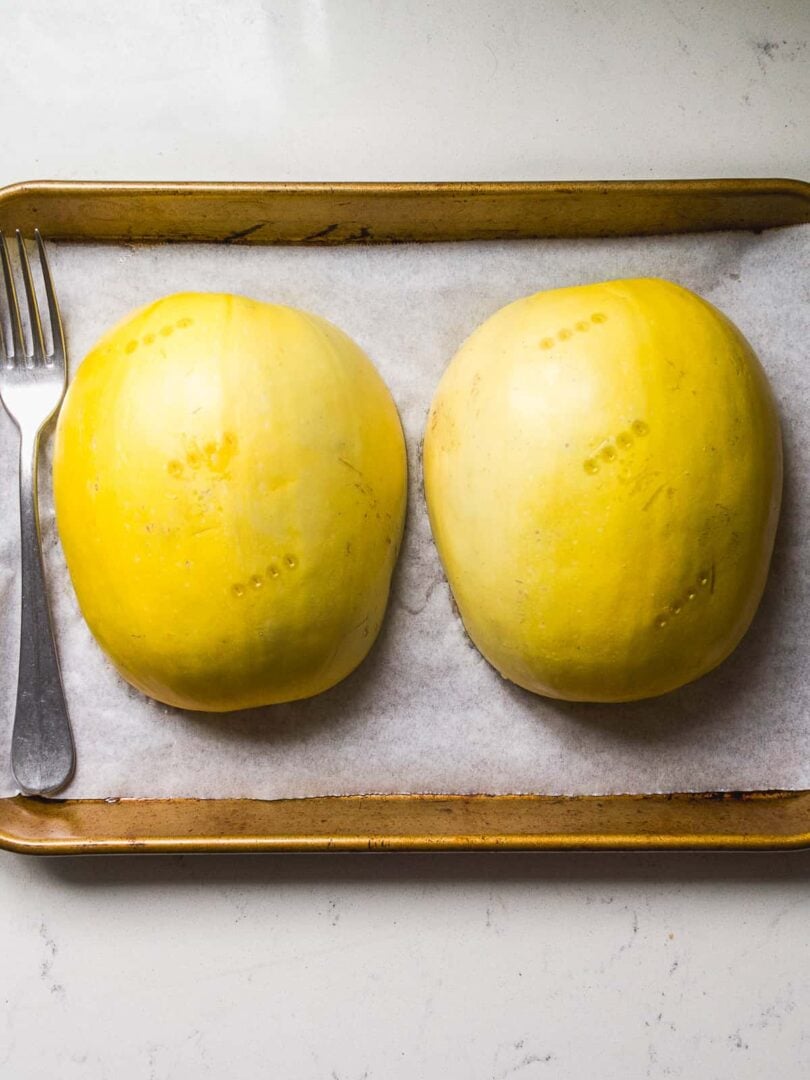 Spaghetti squash halves flipped upside down on a baking pan about to be roasted.