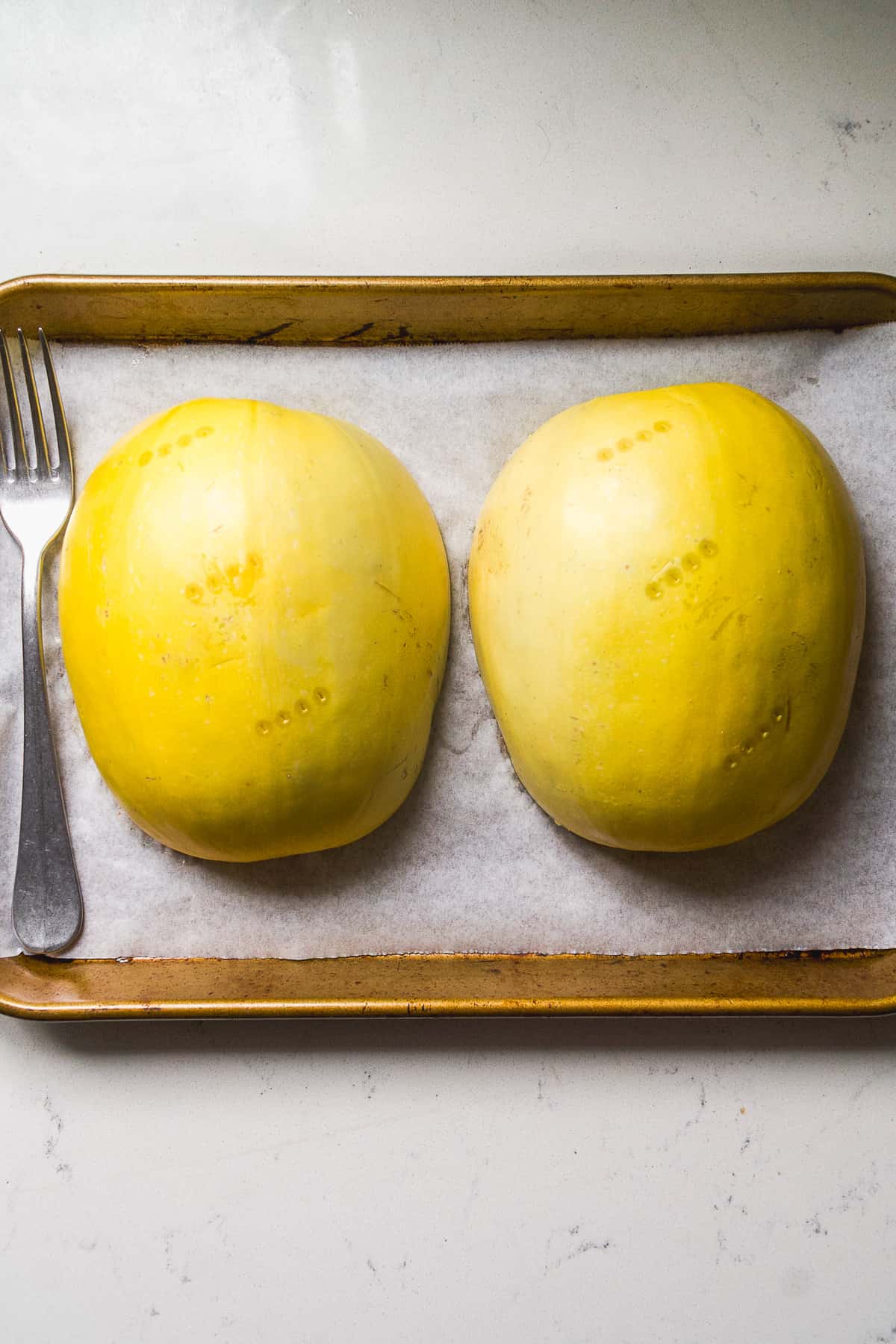 Spaghetti squash halves flipped upside down on a baking pan about to be roasted.