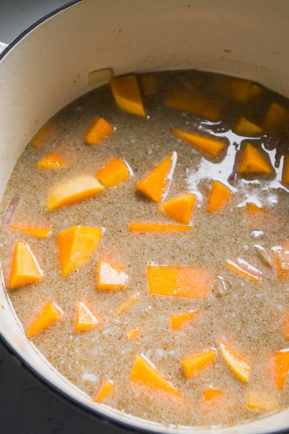 Butternut squash cubes in a pot with broth and coconut milk about to be cooked.