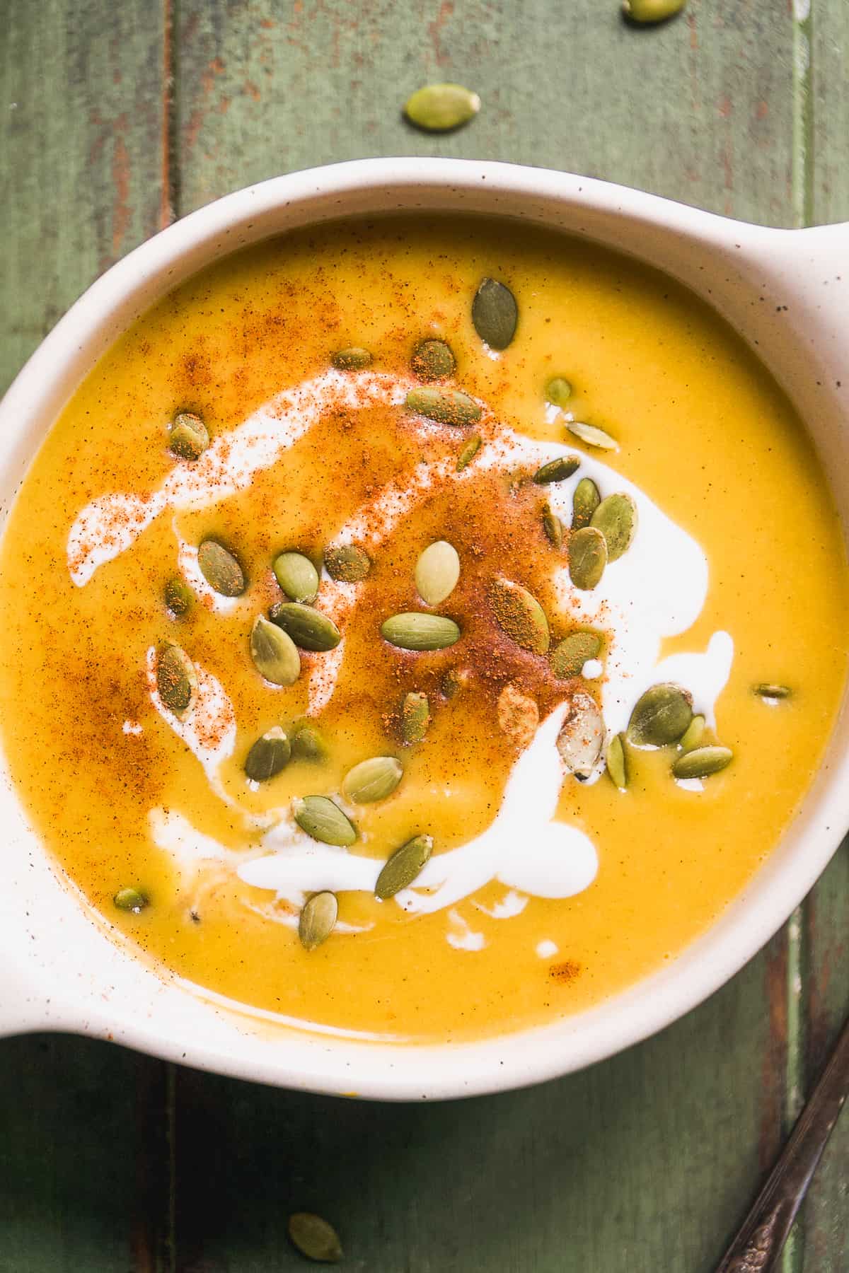 Overhead view of butternut squash in a bowl with pumpkin seeds, cinnamon, and coconut milk drizzled on top.