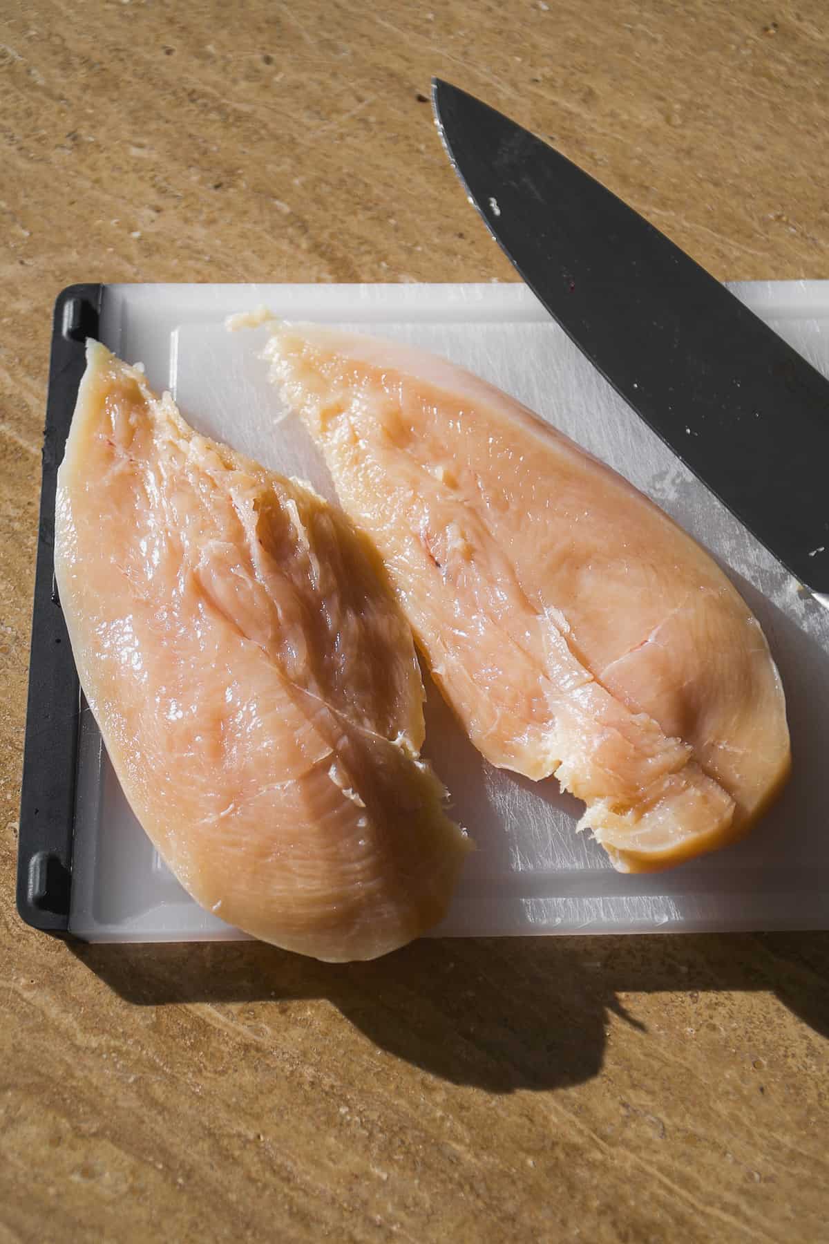 Chicken breast butterflied into two pieces on a cutting board.