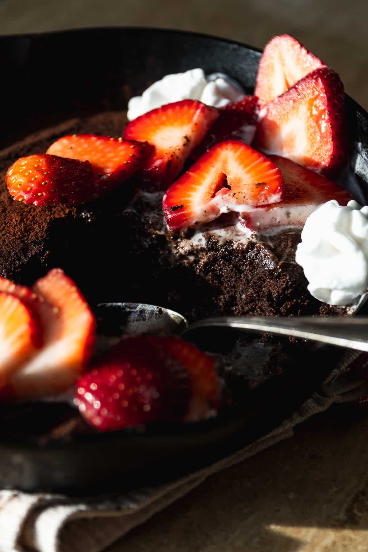Chocolate cake in a cast iron skillet with coconut whipped cream and strawberries.