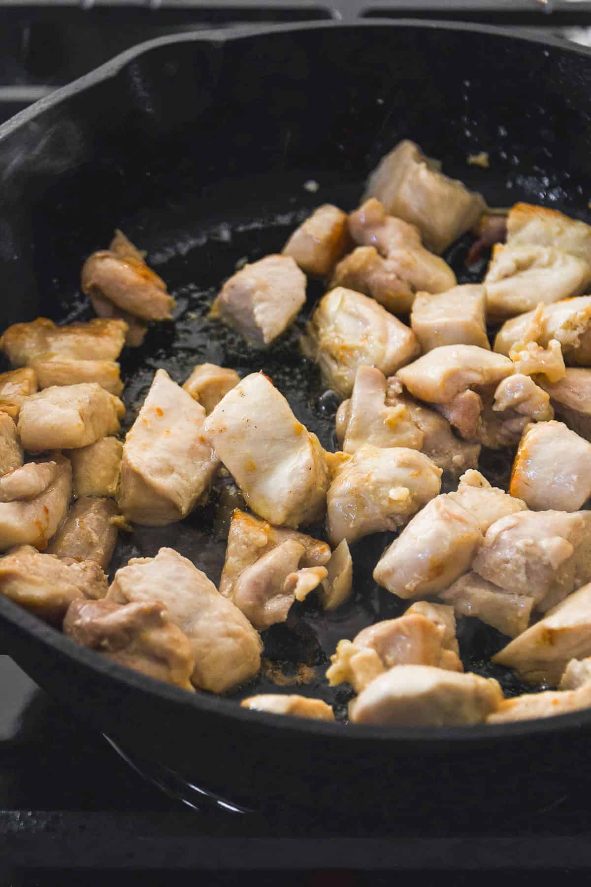 Chicken bites cooking in a cast iron skillet.