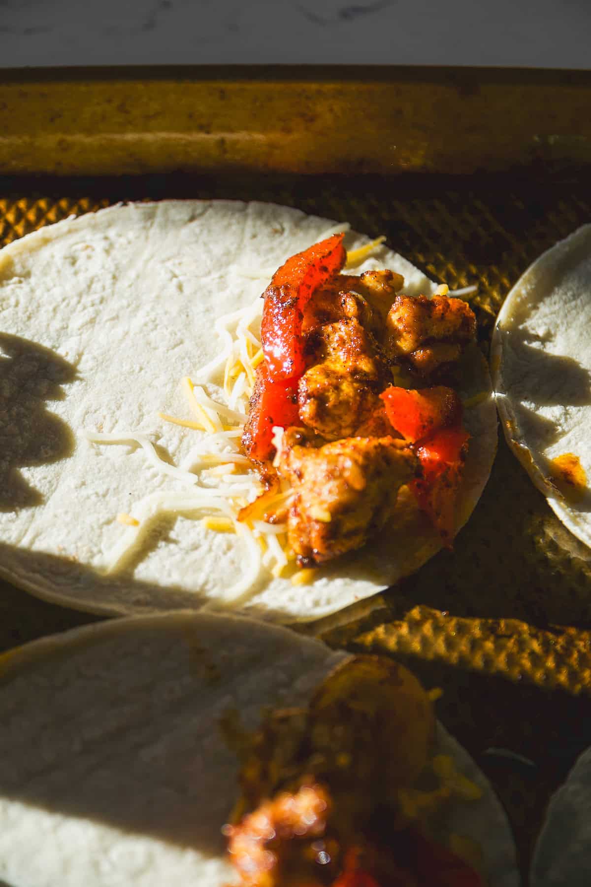 Chicken tacos open on a baking sheet about to be baked.