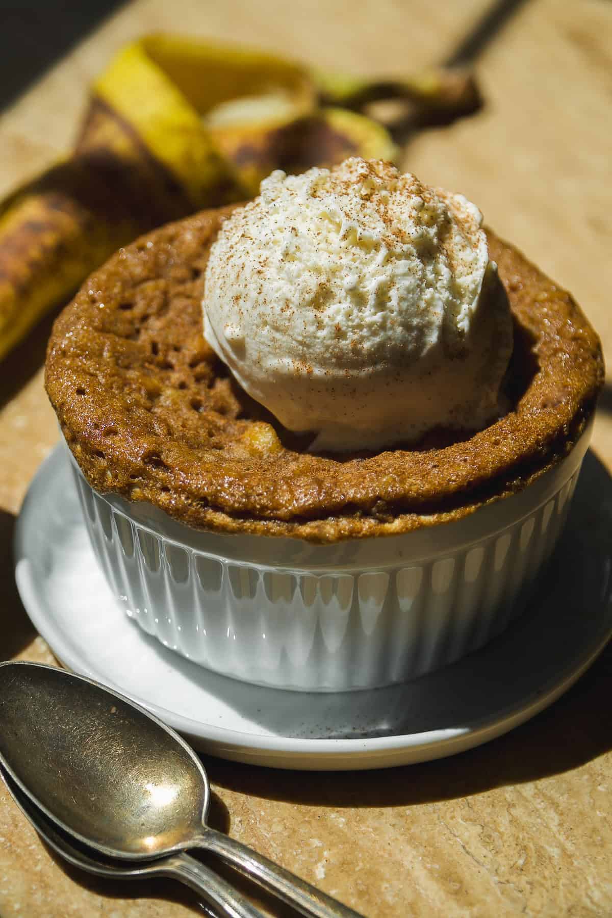 Banana cake in a mug with ice cream on top.