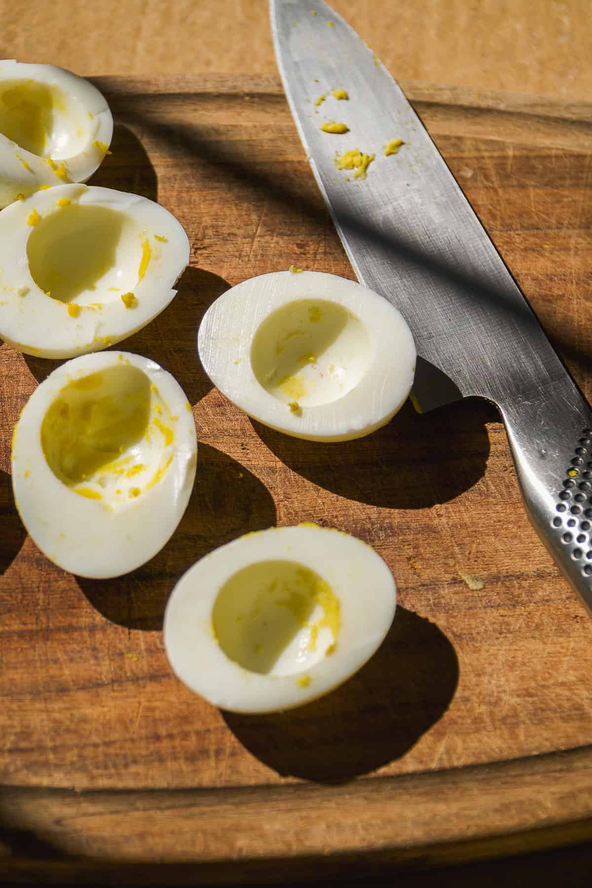 Hard boiled egg whites on a cutting board with a knife.