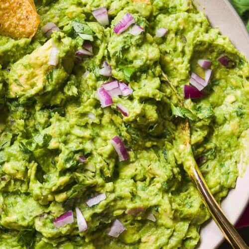 Guacamole in a dip with chips being dipped into the bowl.
