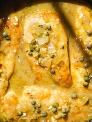 Up close view of chicken piccata in lemon sauce with capers on top.
