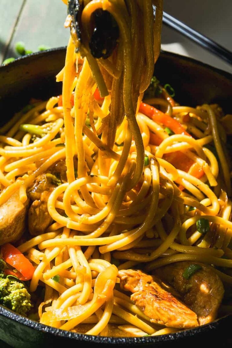Chicken lo mein in a skillet with tongs pulling up some noodles.