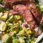 Up close view of a steak salad with avocado and corn.