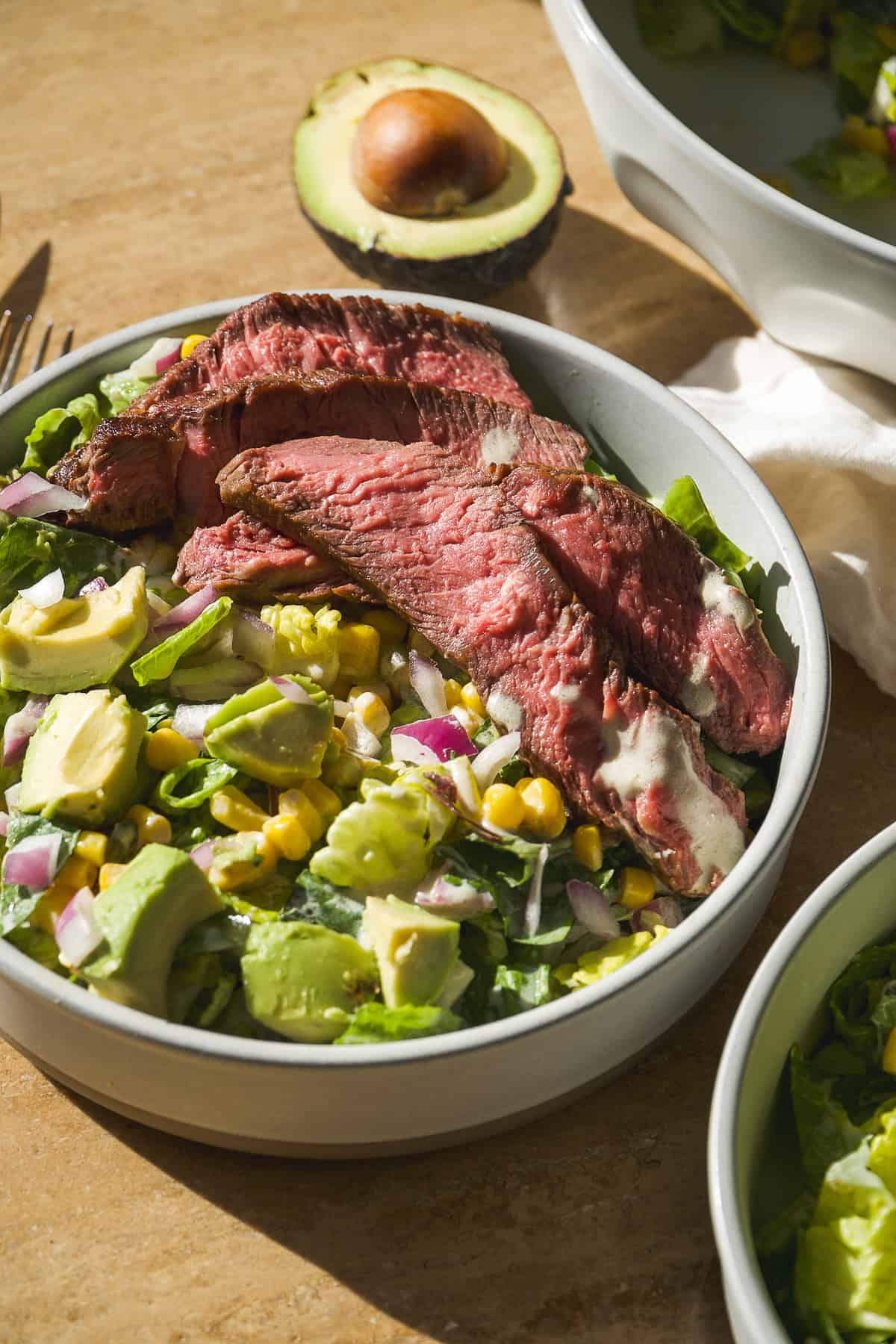 Salad with strips of steak, avocado, corn, and lettuce.