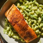Overhead view of basil pesto pasta with a filet of salmon on top.