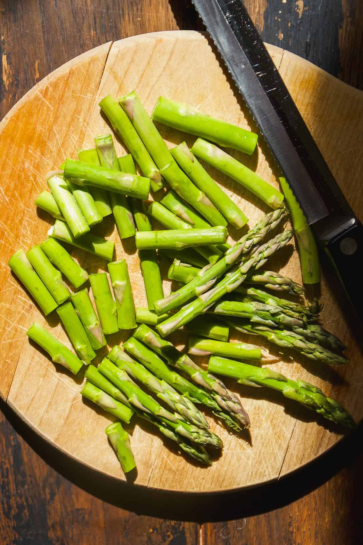 Asparagus cut into pieces on a cutting board with a knife.
