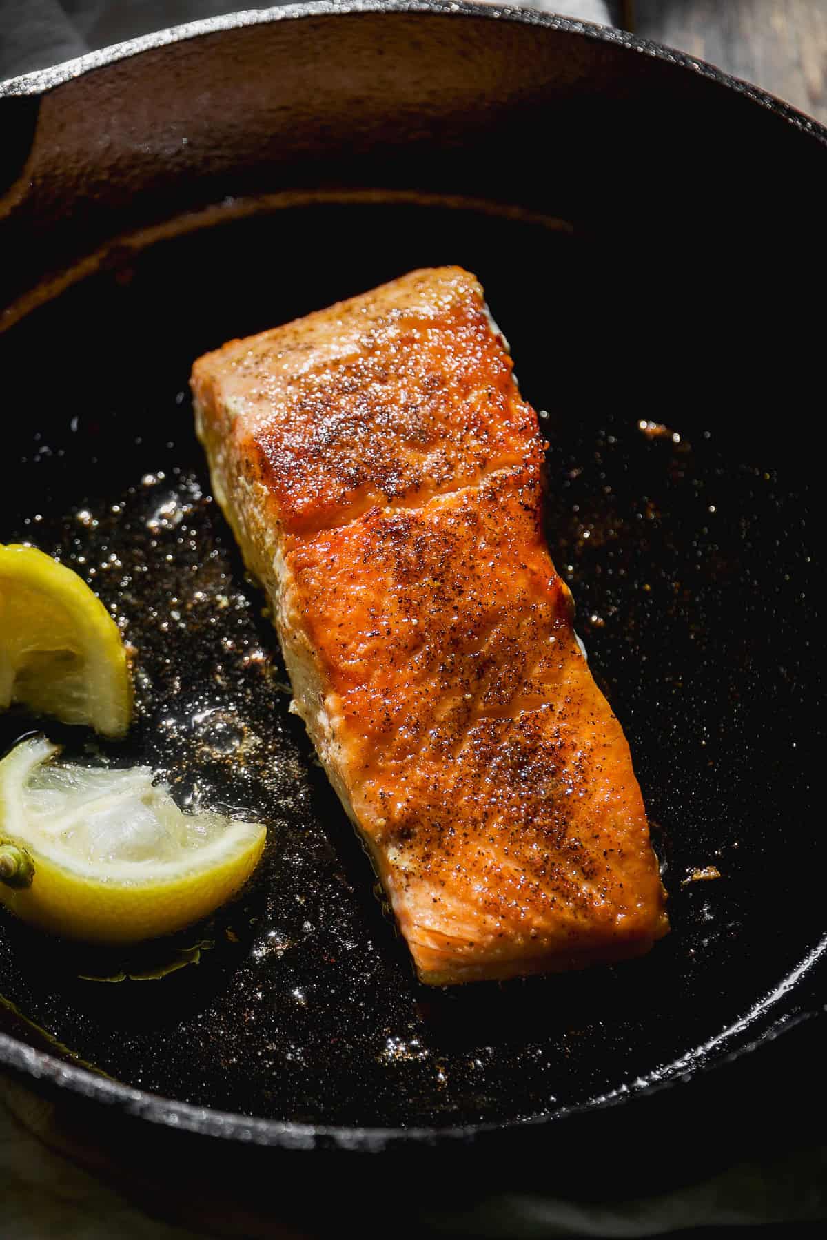 Salmon filet seared in a cast iron skillet with lemon.