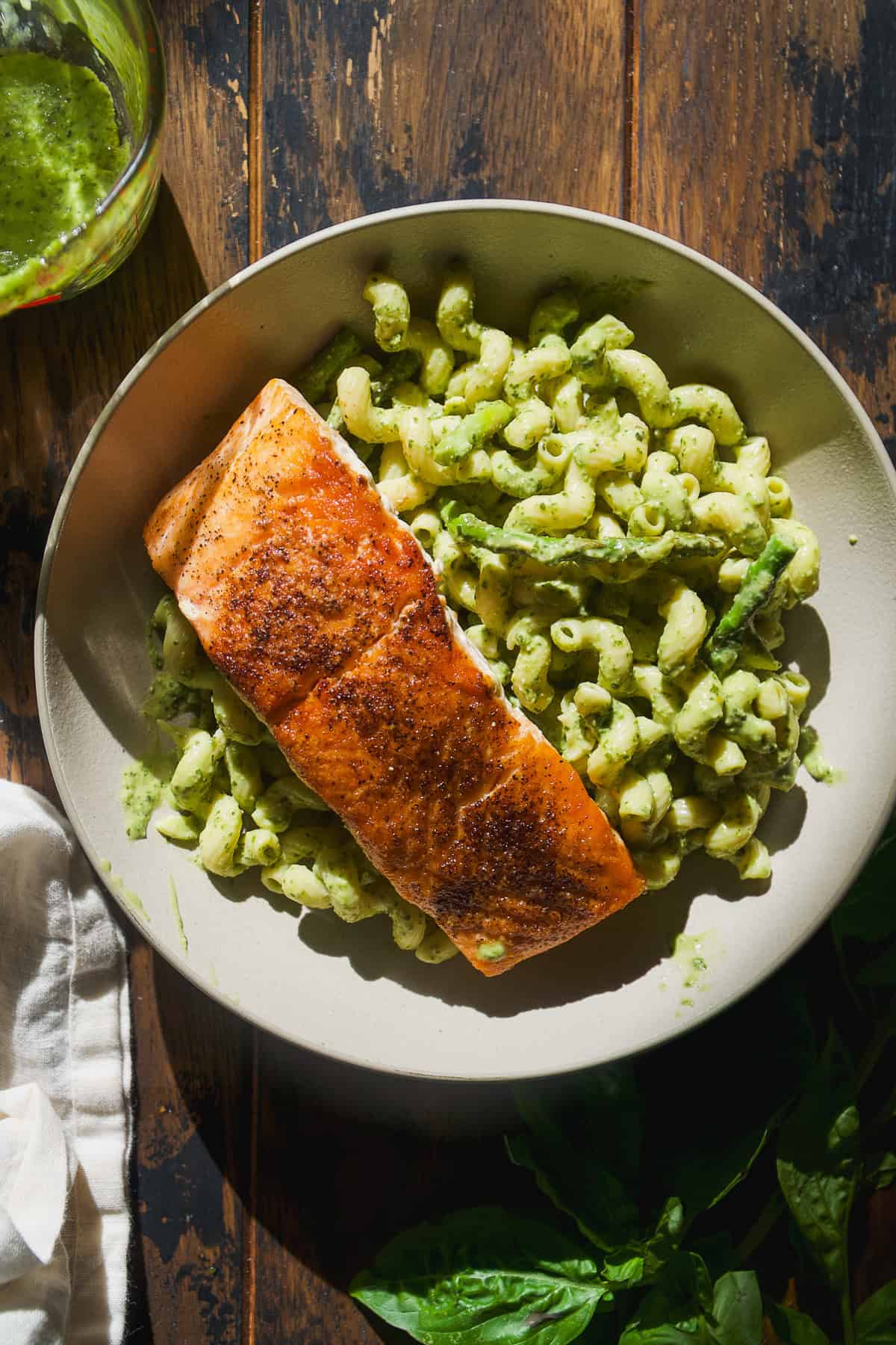 Bowl of pesto pasta with seared salmon on top.
