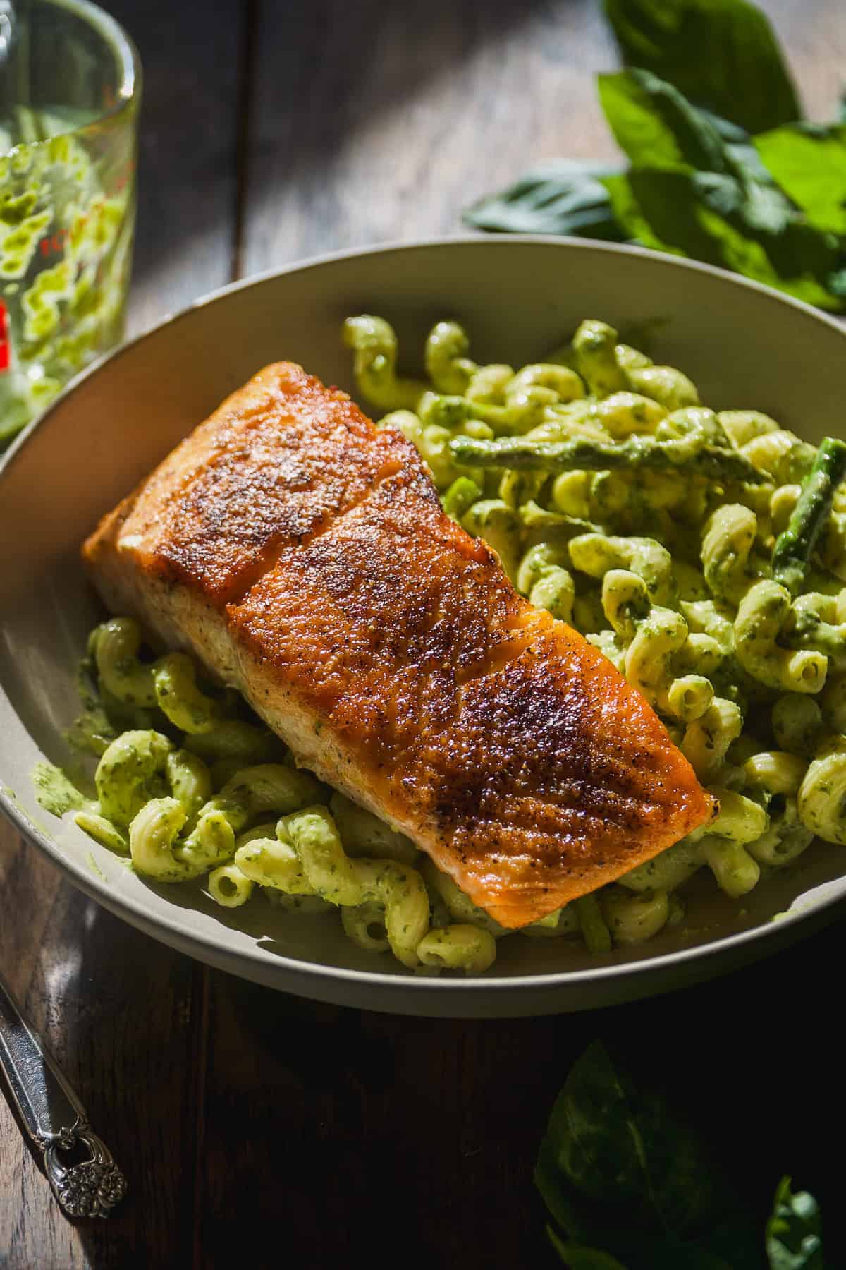 Pesto pasta in a bowl with salmon on top.