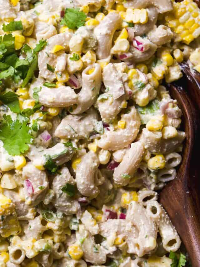 Close-up of a creamy pasta salad with elbow macaroni, corn, red onion, cilantro, and a light dressing, served in a wooden bowl.