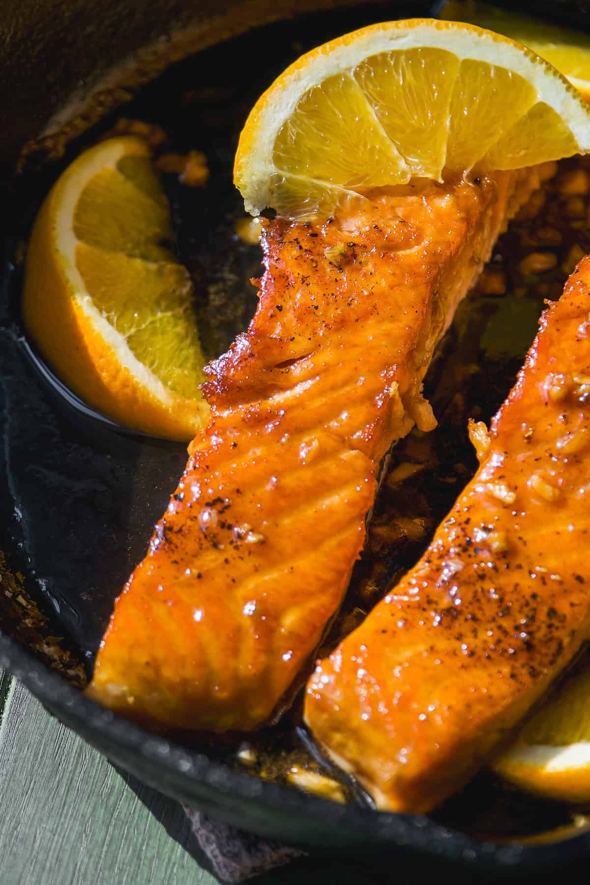 Honey orange salmon in a cast iron skillet with sticky sauce.