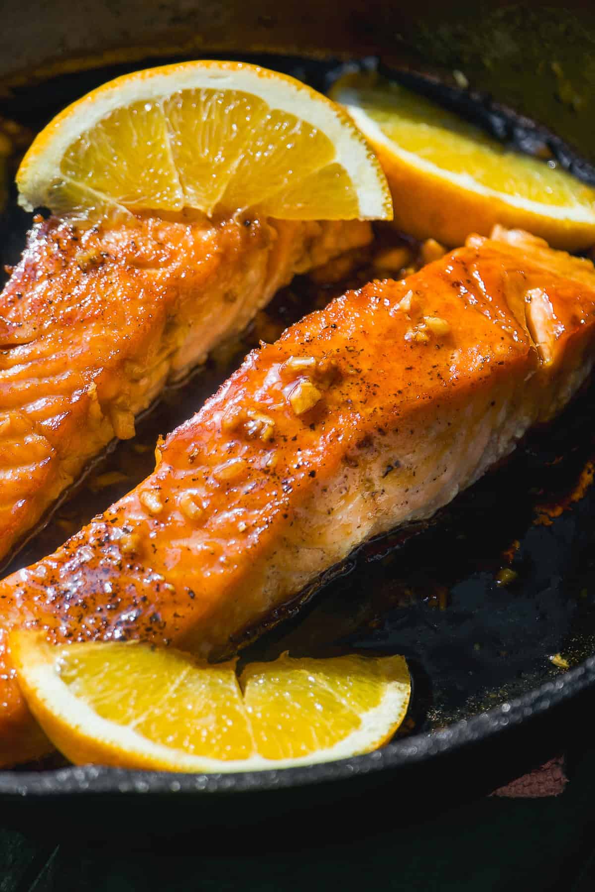 Honey orange salmon in a skillet with orange slices.