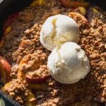 Peach cobbler skillet with two scoops of ice cream on top.