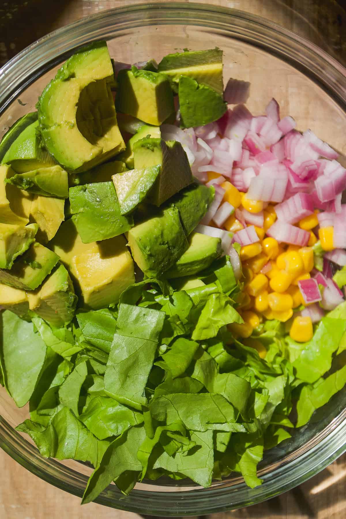 Avocado and lettuce about to be tossed with corn and red onion in a bowl.