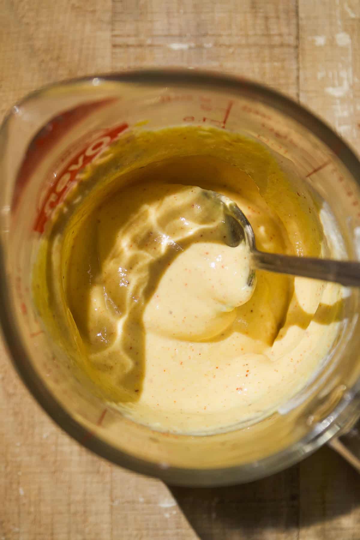 Mustard yogurt dressing mixed in a glass cup with a spoon.