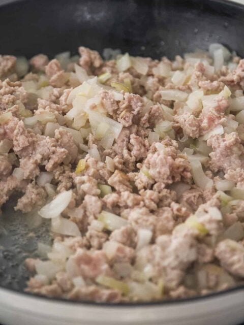 Ground pork cooking in a skillet with onions.