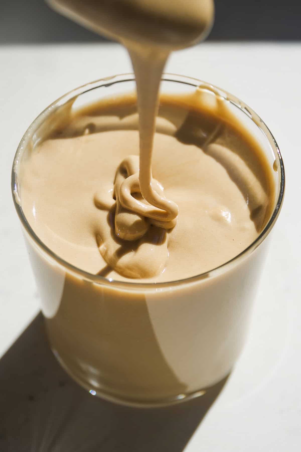 A spoon dripping maple cream into a jar.