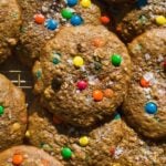 Monster cookies piled on a cooling rack with m&ms.