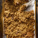 Pumpkin granola on a baking sheet with a wooden spoon.