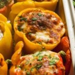 Stuffed peppers in a casserole dish baked with cheese on top.