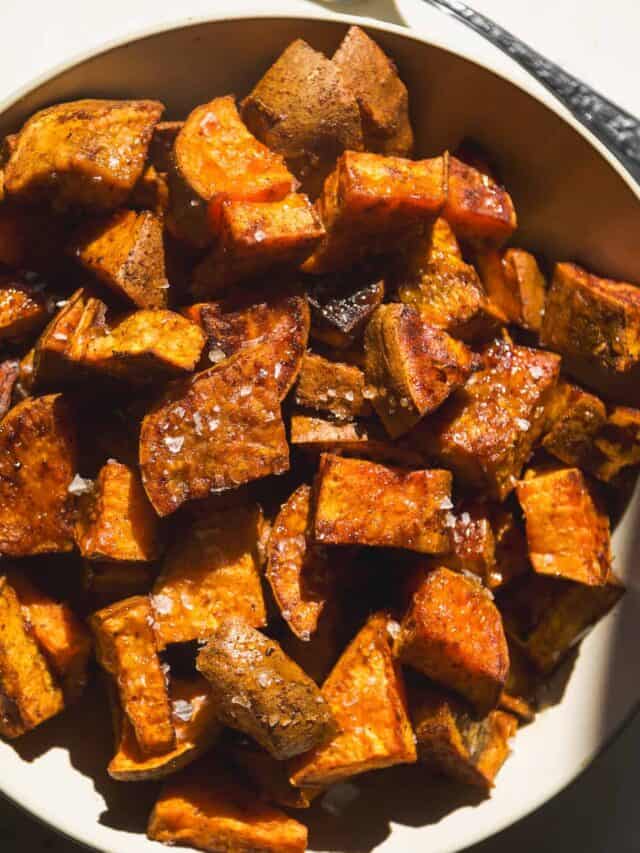 A bowl filled with roasted sweet potato cubes, seasoned and sprinkled with coarse sea salt, shown in warm natural light.