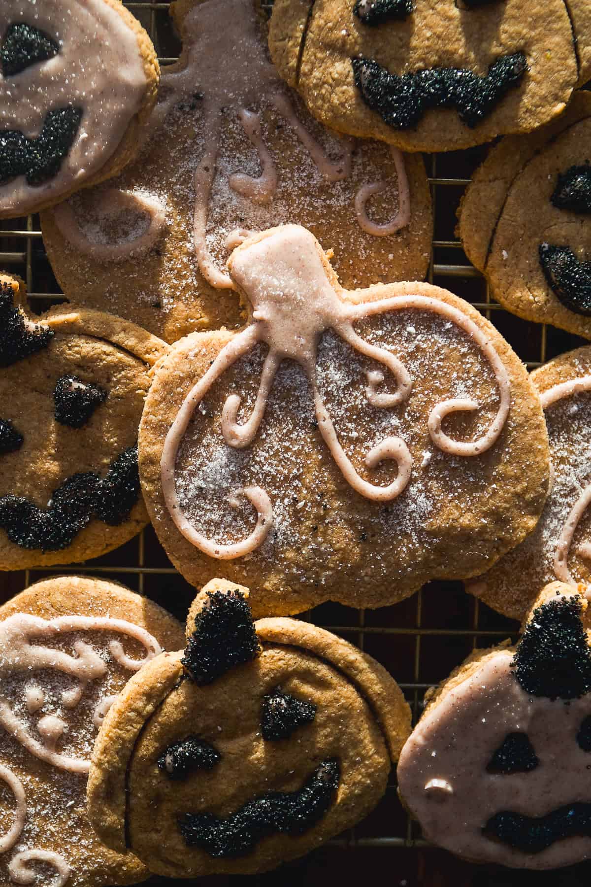 Cut out pumpkin and jack-o-lantern sugar cookies on a wire rack with icing and sprinkles.