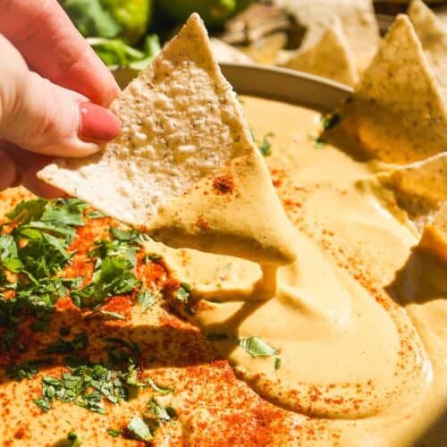 Person dipping a chip in a bowl of cashew queso.
