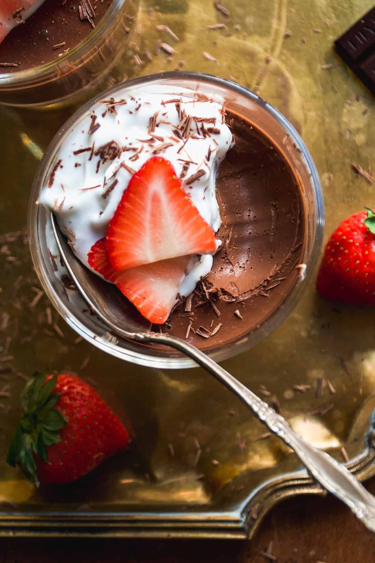 Spoon in a mason jar with chocolate dessert topped with whipped cream, chocolate shavings, and strawberry slices.