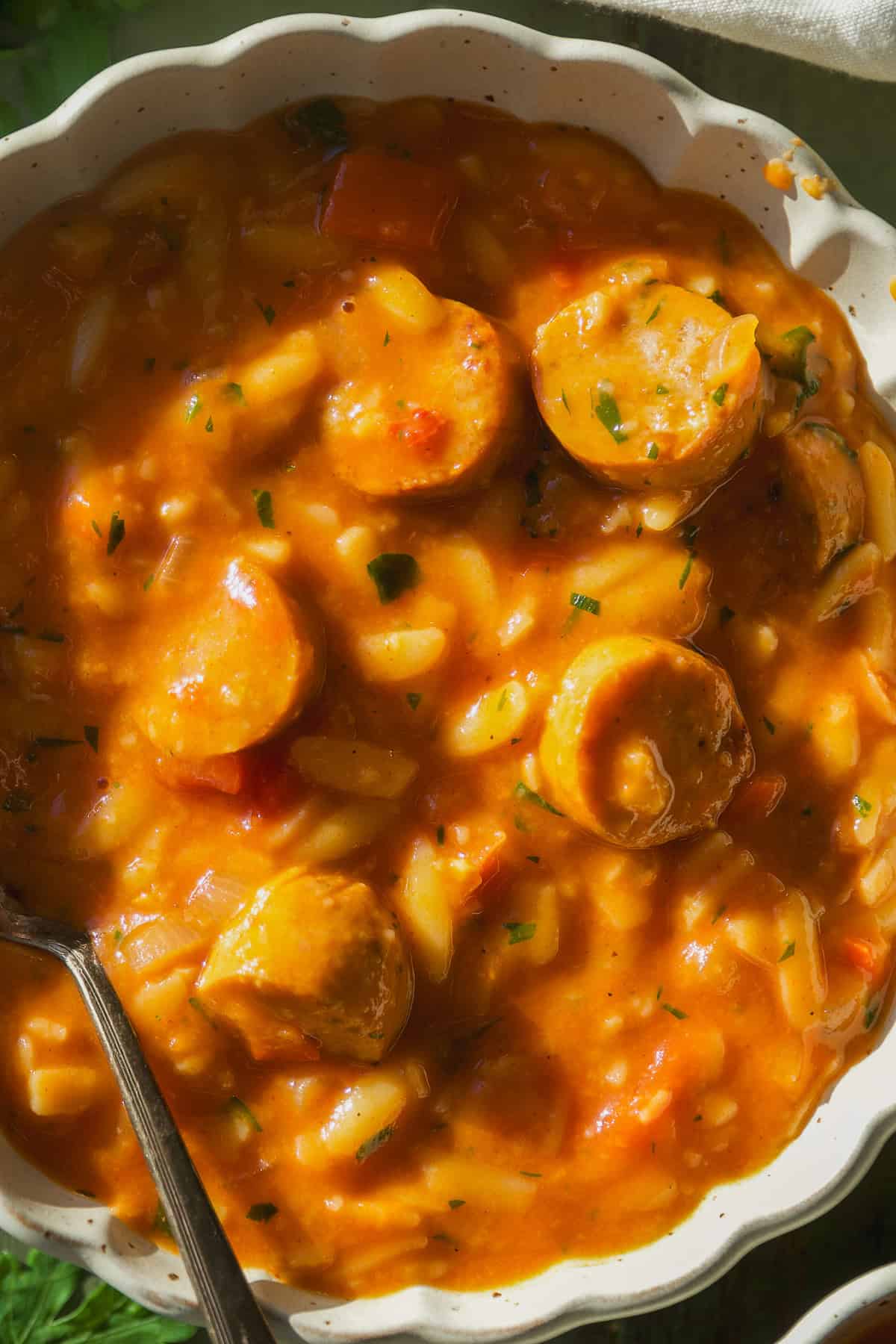 Overhead view of tomato orzo soup with chicken sausage mixed in.