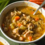 Bowl of creamy chicken and wild rice soup with carrots, celery, and mushrooms on a green surface.