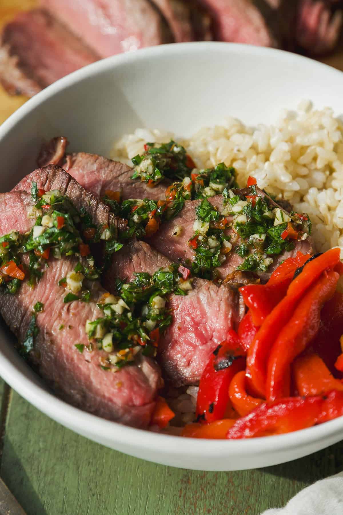 Rice bowls with steak and chimichurri sauce on top and roasted red peppers.
