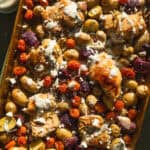 Overhead view of greek sheet pan chicken dinner with herbs and yogurt sauce.