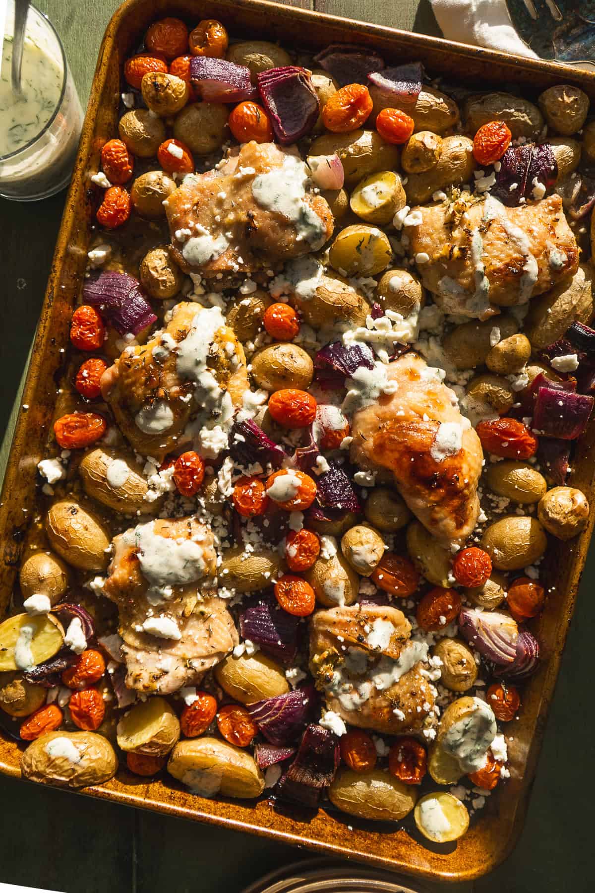 Overhead view of greek sheet pan chicken dinner with herbs and yogurt sauce.