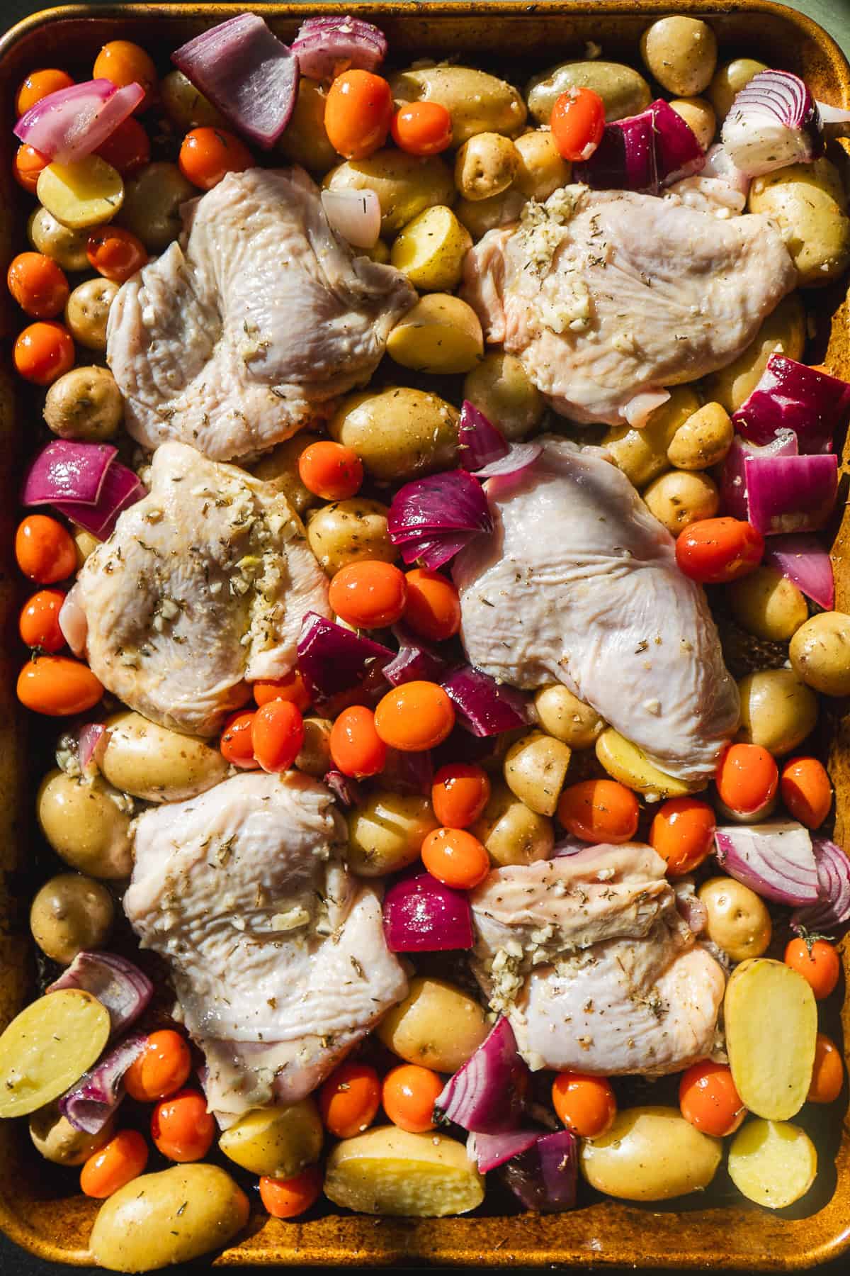 Chicken thighs nestled on a pan with roasted veggies about to be cooked.