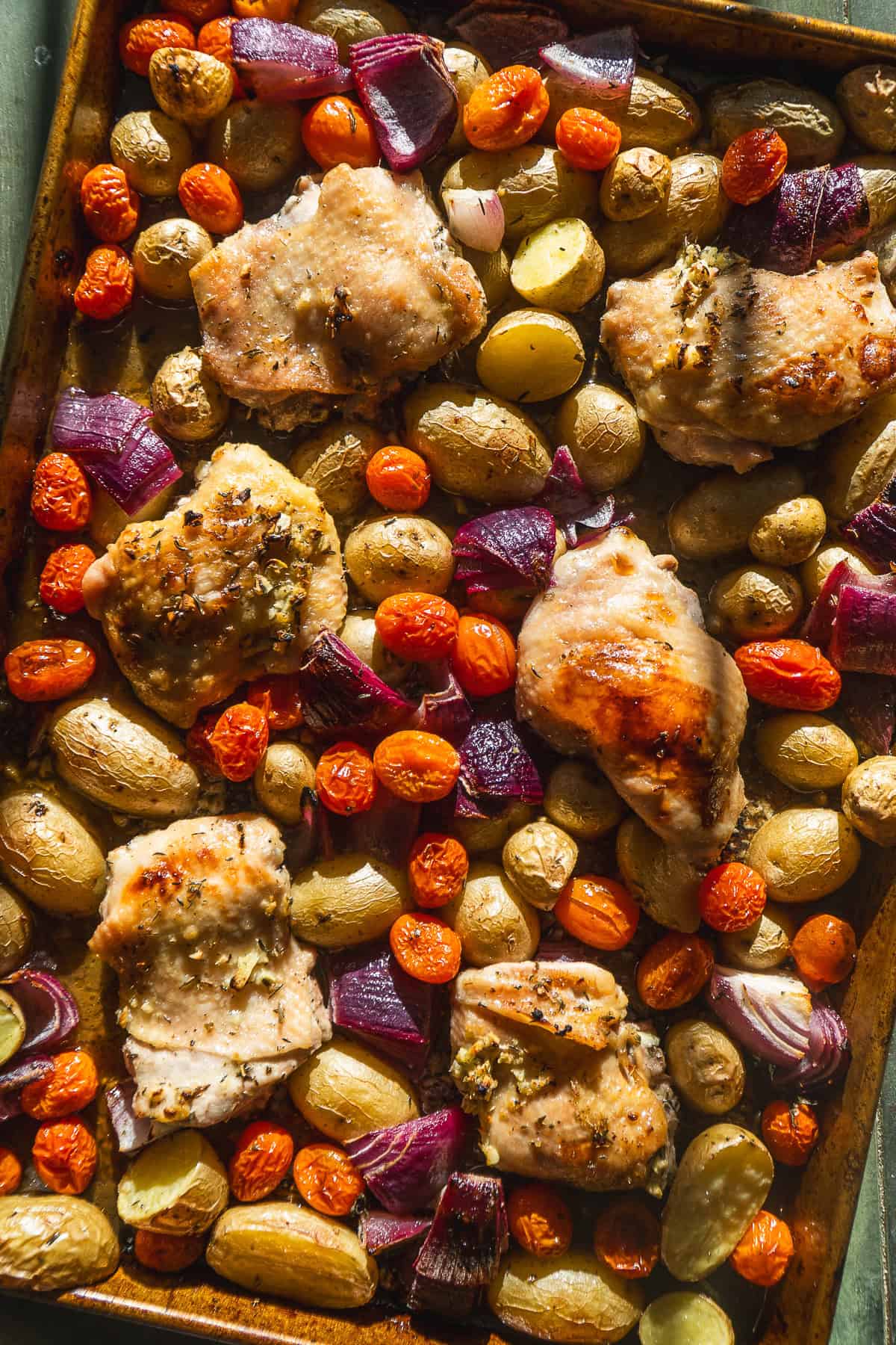 Roasted chicken thighs on a sheet pan with potatoes and vegetables.